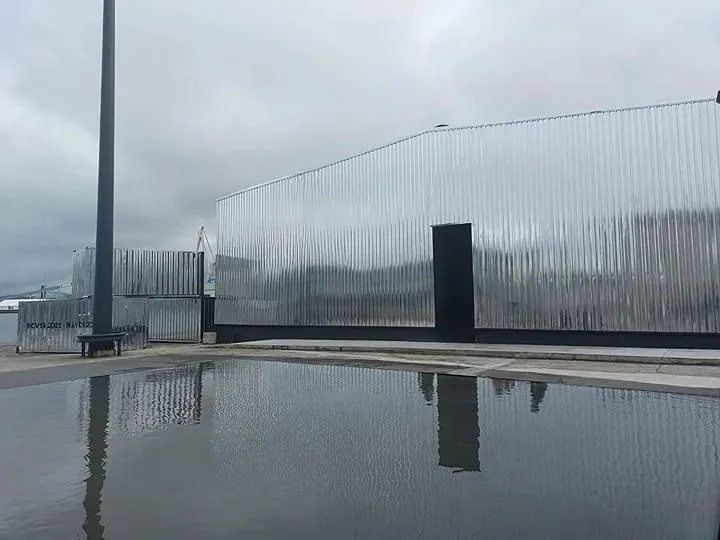 Fachada industrial con chapa grecada de acero inoxidable AISI 304 reflejando el entorno en un día lluvioso